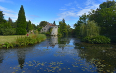 A woman admiring the exterior of a British medieval castle and its reflection in water Exotic gardens with panoramic views of a moated fortress and a Victorian country mansion all in a historic estate