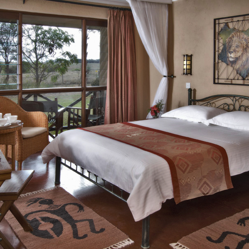 Hotelzimmer in Kenia mit Doppelbett und afrikanischen Dekoelementen.