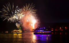 Boote auf einem Fluss bei Nacht mit farbigem Feuerwerk am Himmel.