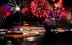 Ein beleuchtetes Schiff mit Feuerwerk am Nachthimmel.