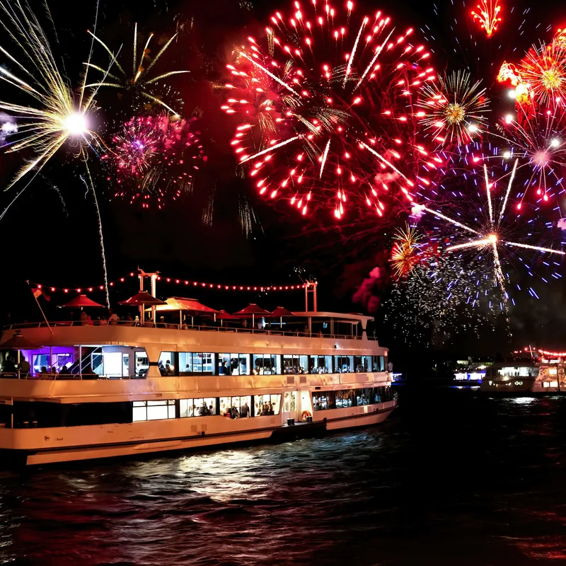 Ein beleuchtetes Schiff mit Feuerwerk am Nachthimmel.