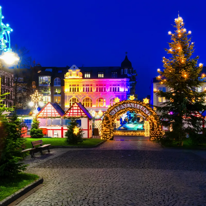 Weihnachtsmarkt am Abend mit bunten Lichtern und geschmücktem Weihnachtsbaum