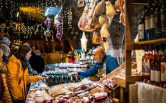 Ein Marktstand mit Wein, Wurst und Käse, besucht von Menschen in einem Keller.