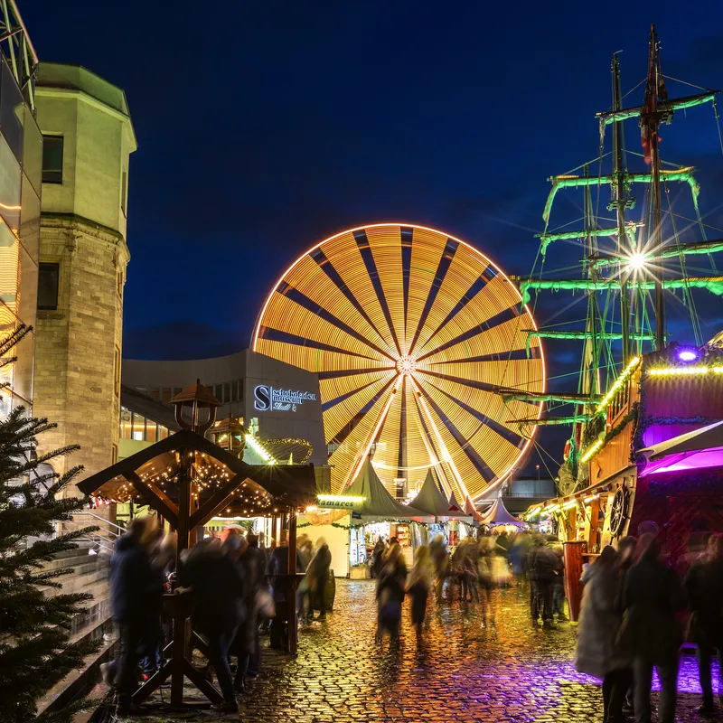 Weihnachtsmarkt am Schokoladenmuseum mit beleuchtetem Riesenrad und Weihnachtsschmuck.