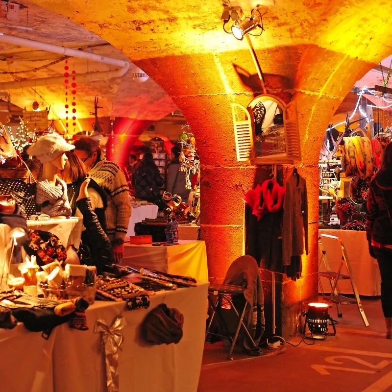 Menschen auf einem stimmungsvoll beleuchteten Weihnachtsmarkt in einem Gewölbekeller.