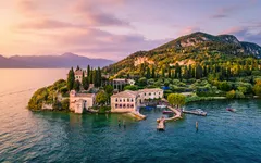 Insel mit historischem Gebäude und Bäumen in einem See bei Sonnenuntergang