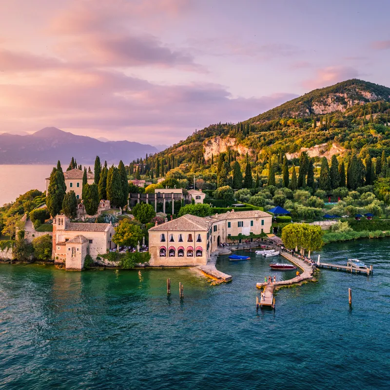Insel mit historischem Gebäude und Bäumen in einem See bei Sonnenuntergang