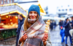 Frau isst auf einem traditionellen deutschen Weihnachtsmarkt mit weißer Schokolade überzogene Früchte am Spieß