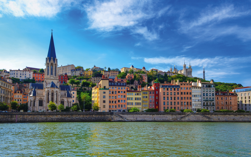 Lyoner Skyline mit Saône, bunten Häusern und Basilika Fourvière bei klarem Himmel.
