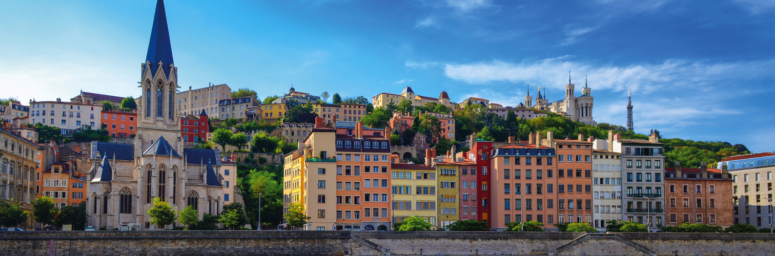 Lyoner Skyline mit Saône, bunten Häusern und Basilika Fourvière bei klarem Himmel.