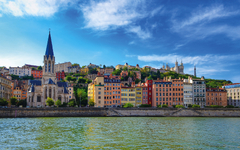 Lyoner Skyline mit Saône, bunten Häusern und Basilika Fourvière bei klarem Himmel.