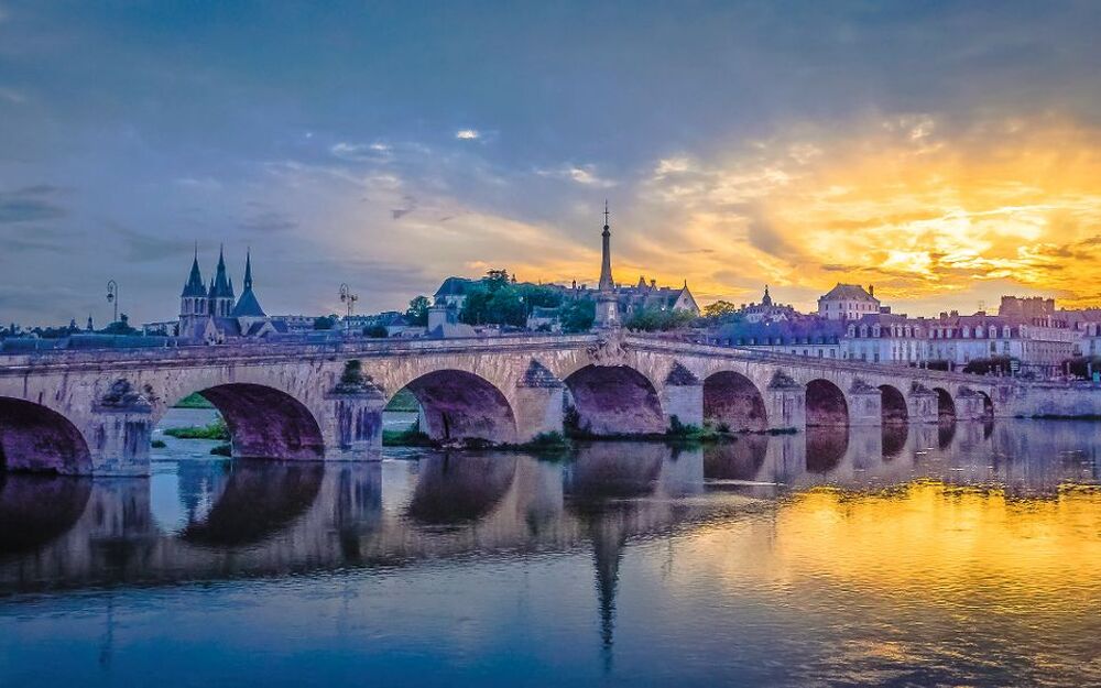 Steinbrücke über einen Fluss bei Sonnenuntergang mit reflektierendem Wasser