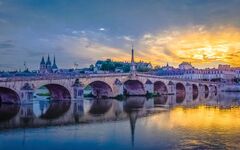 Steinbrücke über einen Fluss bei Sonnenuntergang mit reflektierendem Wasser